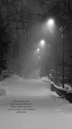 a black and white photo of a snowy path at night with street lights in the distance