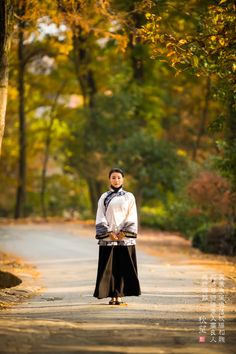 a woman standing on the side of a road with trees in the background and leaves all around her