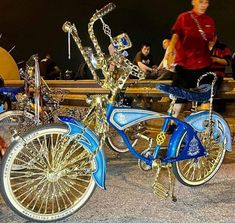 a blue and gold bike is parked in front of a bench with people walking by