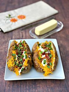 two loaded baked potatoes on a plate with cheese and green onions next to butter cubes