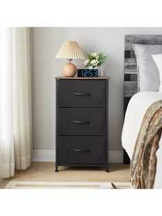 a night stand with two drawers and a clock on it next to a bed in a bedroom