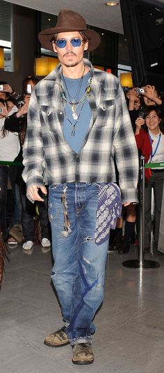 a man wearing a hat and sunglasses is walking through an airport with his hand in his pocket