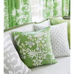 green and white pillows sitting on top of a bed in front of a window with curtains