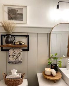 a white toilet sitting in a bathroom next to a sink under a mirror and a wooden shelf