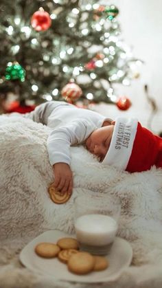 a baby sleeping on a blanket next to a christmas tree with cookies in front of it