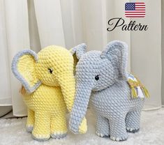 two knitted elephants standing next to each other on a white surface with curtains in the background