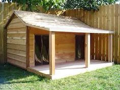 a dog house built into the side of a fenced in area with grass and trees