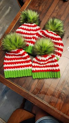 three knitted hats with green and red pom - poms sitting on top of a wooden table