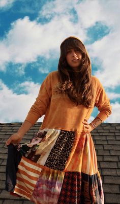 a woman standing on top of a roof with her hands in her pockets and wearing an orange sweater