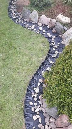 a garden with rocks and water running through the grass, along side a path that leads to a grassy area