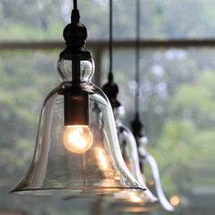 three glass bell lights hanging from a ceiling in front of a window with trees outside