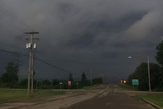 an empty road with storm clouds in the background and street signs on either side,