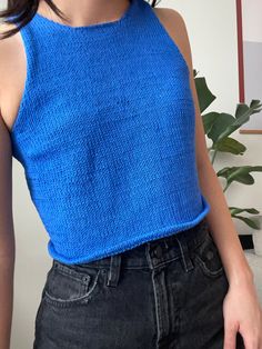 a close up of a person wearing a blue top and black jeans with a plant in the background