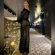 a woman in a long black dress standing on a tiled floor next to a wall