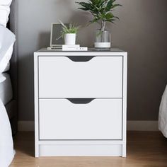 a white nightstand with two drawers and a potted plant next to it on a bed