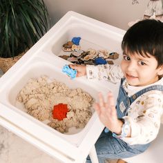 a little boy sitting at a table with his hands in the sand and playing with it