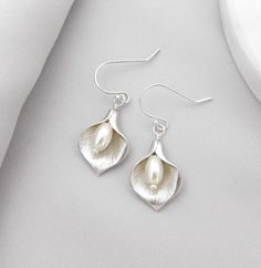 Calla Lily Earrings - Timeless, Simplicity make them so versatile...These earrings look fantastic paired with the matching silver calla lily necklace for an evening out on the town! Perfect for the bride or bridesmaid earrings.   Materials: Calla Lily Earrings: ~ Silver Plated Calla Lily's ~ White Glass Pearl ~ Sterling Silver Ball Ear Wires    ►  Earrings have a 1.25" drop These stunning calla lily earrings are perfect for your bridal jewelry. More Calla Lily Jewelry: https://www.etsy.com/shop/ Calla Lily Jewelry, Lily Earrings, Lily Jewelry, Timeless Simplicity, Lily Necklace, Bridesmaid Pearl Earrings, Pearl Earrings Wedding, Jewelry White, Earrings Bridesmaid