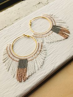 two pairs of gold and white beaded hoop earrings on top of a piece of wood