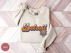 Show your love for the Detroit baseball with this cozy and stylish apparel. Perfect for baseball season, this crewneck sweatshirt, t-shirt, and hoodie come in white, orange, navy, natural, and sport grey options. Order now to stay warm and support Tigers baseball in style! Printing: This item features Direct-To-Garment printing, ensuring durability without cracking or peeling like vinyl. Ink is integrated into the fabric, providing a lasting print that doesn't sit on the surface. Care Instructio Letter Print Sweatshirt For Baseball Season Streetwear, Crew Neck Sweatshirt For Baseball Season Streetwear, Crew Neck Sweatshirt For Streetwear And Baseball Season, Baseball Season Crew Neck Hoodie With Graphic Print, Baseball Season Graphic Print Crew Neck Hoodie, Baseball Season Crew Neck Sweatshirt With School Spirit, School Spirit Sweatshirt With Crew Neck For Baseball Season, School Spirit Crew Neck Sweatshirt For Baseball Season, Crew Neck Sweatshirt For Baseball Season With School Spirit