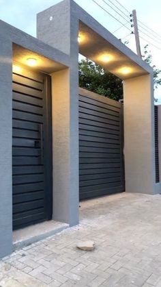 two tall gray buildings sitting next to each other on a brick sidewalk with lights above them