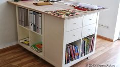 a desk with books on it in the middle of a wooden floored area next to a wall