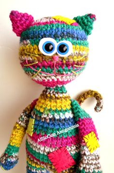 a crocheted cat with big blue eyes sitting on top of a white wall