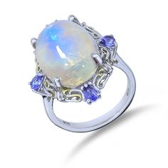 "**All photos are professionally photographed in our in-house studio, and are of the exact item you will receive.** **All measurements done in inches are rounded to the nearest 1/8\". ** The ethereal blue phenomenon of a moonstone is nicely paired with 4 tanzanite in the sterling silver halo setting on this ring. Metal Type: Sterling Silver Hallmarks: 925, STS Metal Finish: High Polish Ring Size: 8.25 Setting: Prong Item Weight: 6.50 grams Center Gemstone Gemstone: Moonstone Shape: Oval Cabochon Formal Opal Moonstone Ring, Oval Opal And Moonstone Multi-stone Ring, Oval Opal Multi-stone Ring With Moonstone, Tanzanite Ring With Gemstone Accents, Tanzanite Rings With Gemstone Accents, Formal Blue Moonstone Ring In Sterling Silver, Blue Moonstone Ring In Sterling Silver For Formal Occasions, Elegant Blue Hallmarked Moonstone Ring, Silver Multi-stone Moonstone Ring