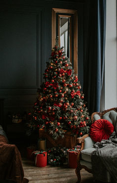 a decorated christmas tree sitting next to a window in a living room with dark walls