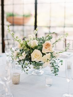 a vase filled with white flowers sitting on top of a table next to wine glasses