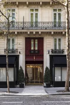 the entrance to a hotel with red shutters and black awnings, surrounded by trees