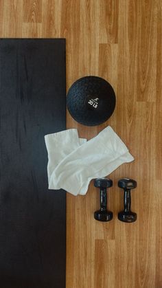 an exercise mat, dumbbells, and towel on a wooden floor next to each other