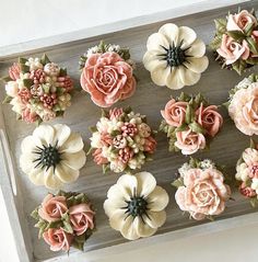 twelve cupcakes decorated with pink and white flowers on a wooden tray, ready to be eaten