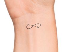 a small wrist tattoo with an infinite symbol on the left side of the wrist, in black ink