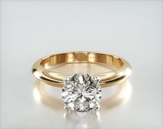 a gold engagement ring with a round diamond in the center, on a white surface