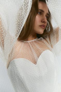 a woman wearing a white dress and veil with polka dots on the fabric behind her