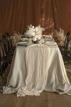 the table is set with an elegant centerpiece and white linens on it, along with black chairs