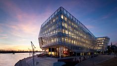 a large glass building sitting on the side of a river next to a dock at sunset