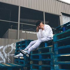 a man sitting on top of blue pallets talking on a cell phone and holding his hand to his face