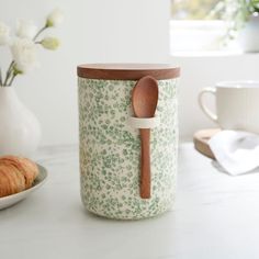 a wooden spoon sitting inside of a jar on top of a counter next to a plate with croissants