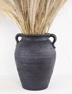 a black vase with some dry grass in it