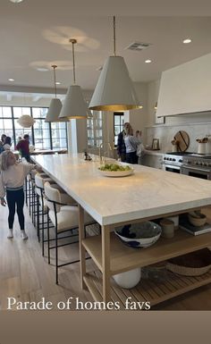 people are standing in the middle of a large kitchen with white counter tops and wooden flooring