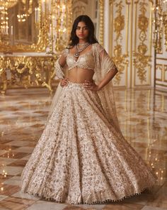 a woman in a white and gold lehenga with her hands on her hips