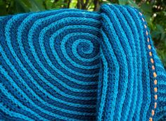 a blue knitted blanket with an orange stitch on the end and green leaves in the background