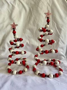 two christmas trees made out of beads on a white sheet with red and white balls