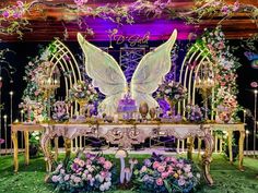 an elaborately decorated table with angel wings and flowers in the center is surrounded by greenery