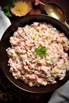 a bowl filled with tuna salad next to two spoons and some parsley on the side