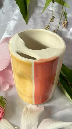 a vase sitting on top of a white table next to pink and yellow flowers with green leaves