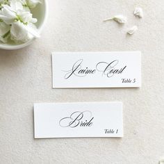 two place cards sitting on top of a table next to a vase with white flowers