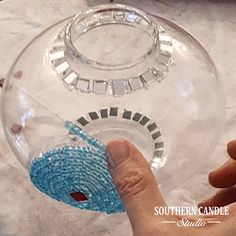 a hand is holding a beaded object in front of a glass bowl on a table