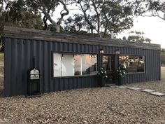 a black shipping container sitting on top of a gravel field next to trees and bushes